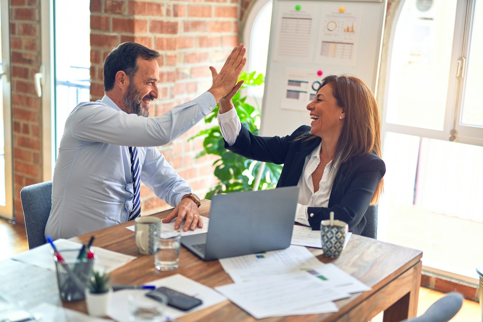 A business owner and consultant high-five across a desk after a planning session
